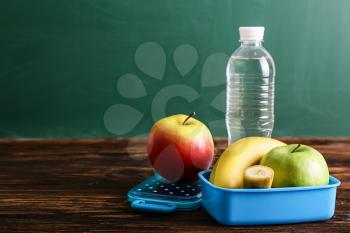 School lunch box with tasty food and bottle of water on table�