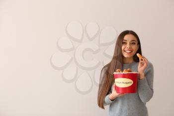 Young woman with bucket of tasty nuggets on light background�