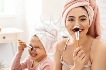 Young mother with cute daughter doing makeup at home�