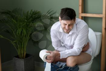 Man suffering from diarrhea while sitting on toilet bowl at home�