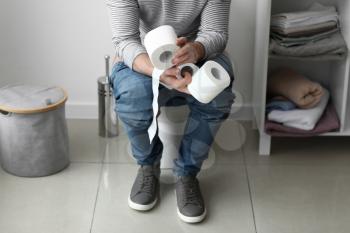 Man with rolls of paper sitting on toilet bowl at home�
