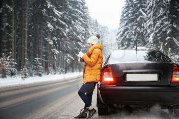 Young woman with hot drink near car at resort on winter day�