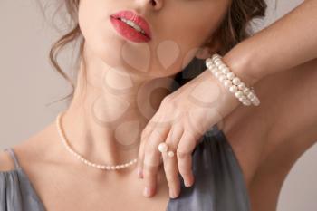 Young woman with beautiful pearl jewelry on light background, closeup�