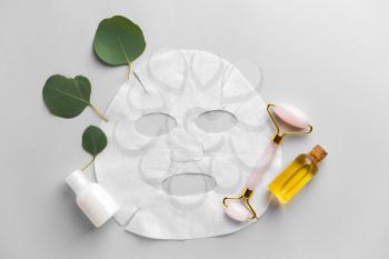 Sheet facial mask with cosmetic products and massage tool on light background�