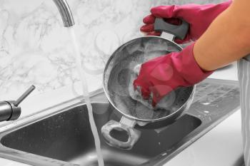 Woman washing saucepan in kitchen sink�