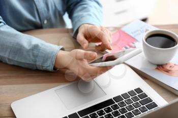 Young woman with mobile phone, laptop and cup of coffee at table�