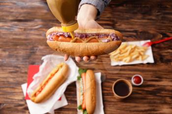 Woman squeezing mustard from bottle onto tasty hot dog�