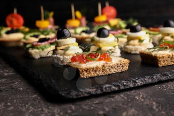 Slate plate with tasty canapes on dark table, closeup�