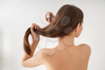 Woman using cosmetics for hair care on white background�