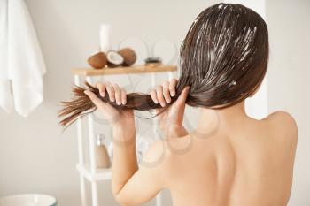 Woman using coconut oil for hair in bathroom�