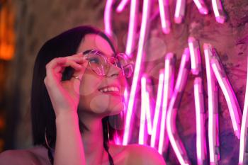 Toned portrait of beautiful young woman near neon lighting on wall�