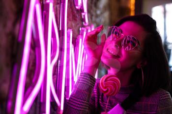 Toned portrait of beautiful young woman near neon lighting on wall�