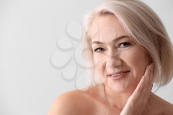 Mature woman giving herself face massage on light background�