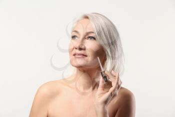 Mature woman applying face serum on light background�