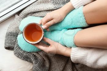 Young woman with cup of hot tea sitting on windowsill at home�