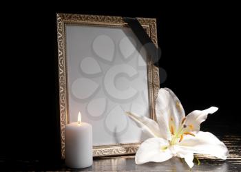 Blank funeral frame, burning candle and flower on table against dark background�