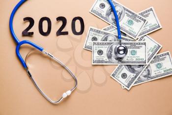 Stethoscope, money and figure 2020 on color background�