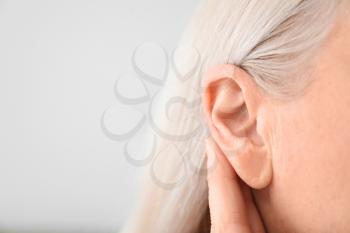 Mature woman with hearing problem on light background, closeup�