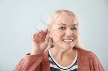 Mature woman with hearing aid on light background�