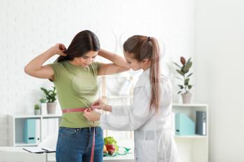 Nutritionist measuring waist of young woman in weight loss clinic�