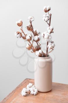 Vase with cotton branches on table against light background�