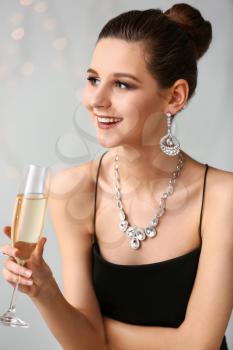Young woman with beautiful jewelry and glass of champagne on light background�