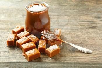 Tasty salted caramel in jar with candies on wooden table�