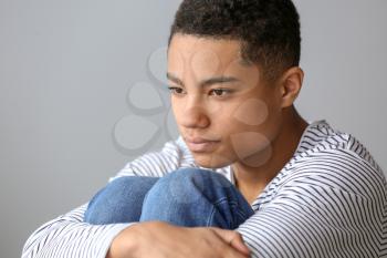 Sad African-American teenage boy on grey background�