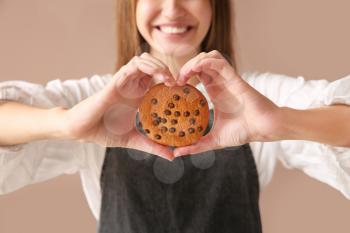 Beautiful female baker with tasty cookie on color background, closeup�