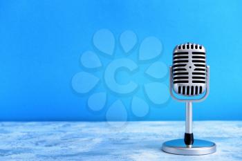 Retro microphone on table against color background�