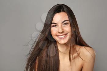 Portrait of beautiful young woman with healthy long hair on grey background�