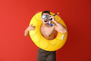 Handsome man with inflatable ring and snorkeling mask on color background�