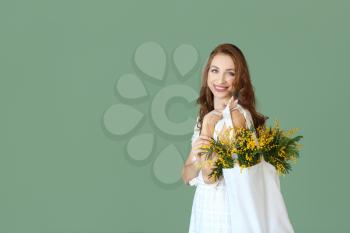 Beautiful young woman holding bag with mimosa flowers on color background�