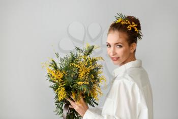 Beautiful young woman with bouquet of mimosa flowers on light background�