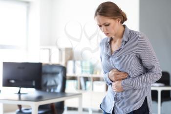 Young woman suffering from stomachache in office�