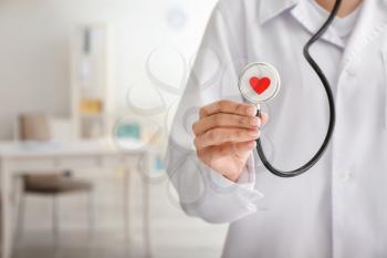 Cardiologist holding stethoscope with red heart in clinic, closeup�