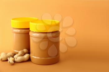 Tasty peanut butter in jars on color background�