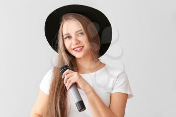Beautiful female singer with microphone on light background�