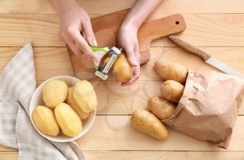 Woman peeling raw potato at wooden table�