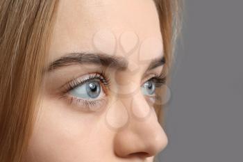 Beautiful young woman with laminated eyelashes on grey background, closeup�