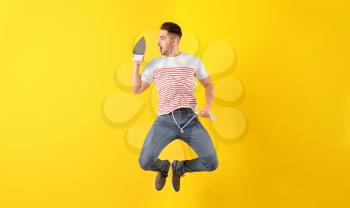 Jumping young man with iron on color background�