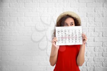 African-American woman holding calendar with marked days of menstruation on white background�