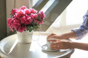 Woman drinking tea at table with beautiful blooming azalea�