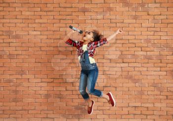 Jumping little African-American singer against brick wall�