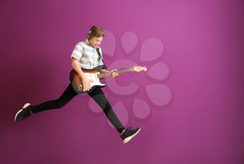 Teenage boy playing guitar against color wall�