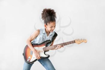 African-American girl playing guitar against light background�