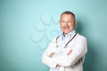Handsome middle-aged doctor on color background�