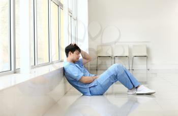 Depressed male medical assistant sitting near window in clinic�