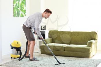 Young man hoovering carpet at home�