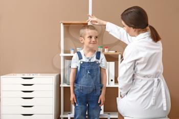 Female doctor measuring height of little boy in hospital�